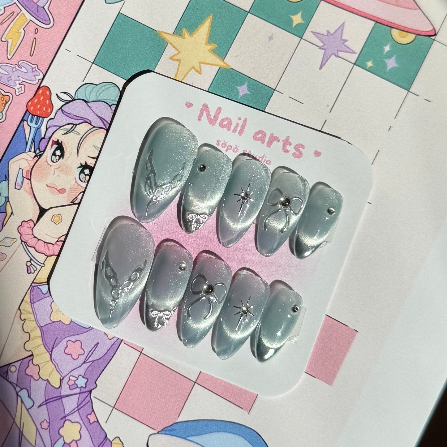 Set of silver nail art decorations on a branded card with a colorful background