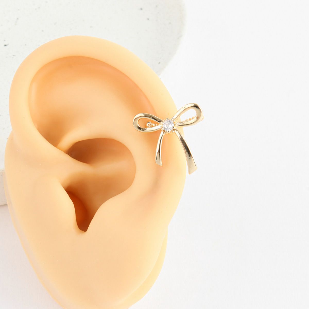 Gold bow-shaped earring on a person's ear with a plain background
