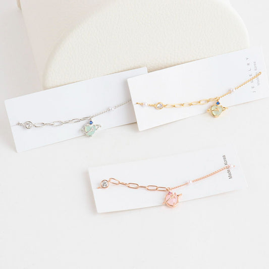 Three gold bracelets on white card holders with a soft beige background