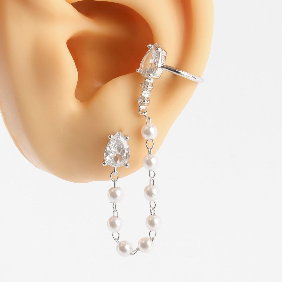 Pearl and crystal earring worn on an ear with a plain background