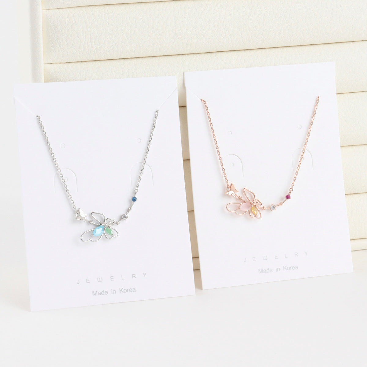 Two butterfly-themed necklaces on white cards with 'Made in Korea' text.