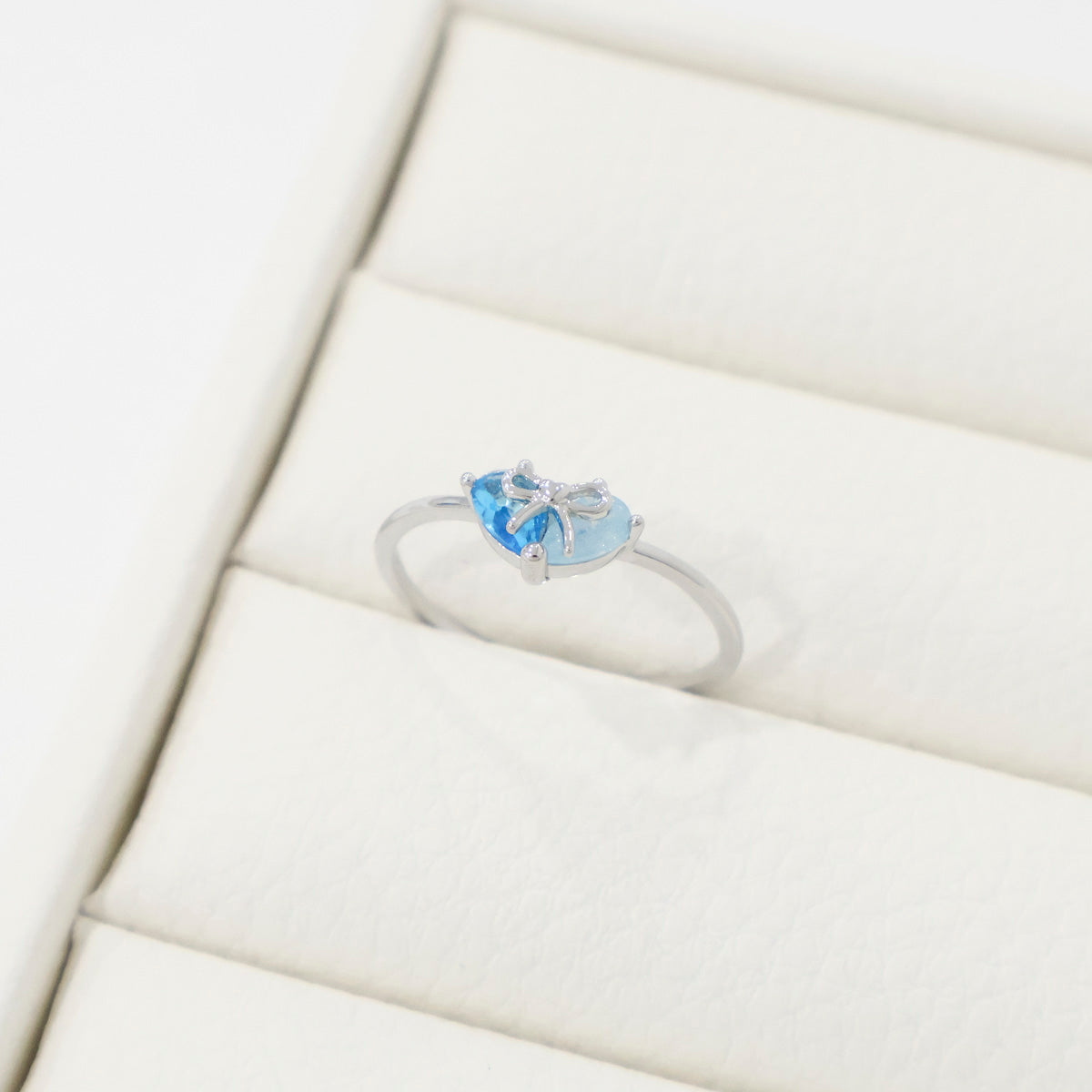 Silver ring with blue gemstone on a white cushion