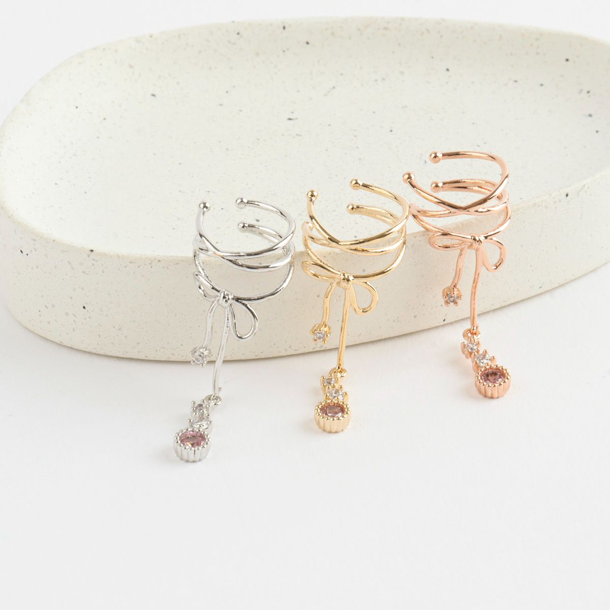Three pairs of earrings in silver, gold, and rose gold on a white surface.