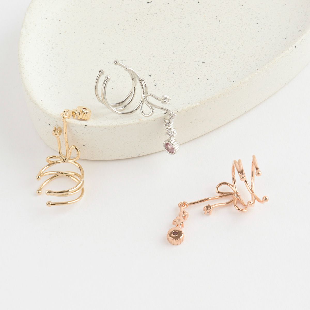 Three pairs of earrings on a white surface with a stone-like background