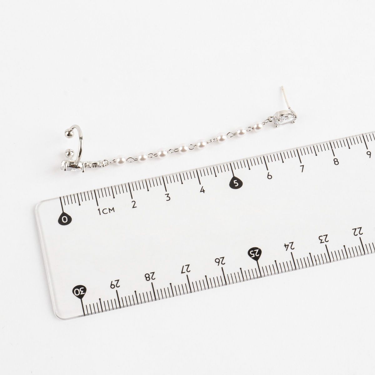 Silver bracelet being measured against a ruler on a white background