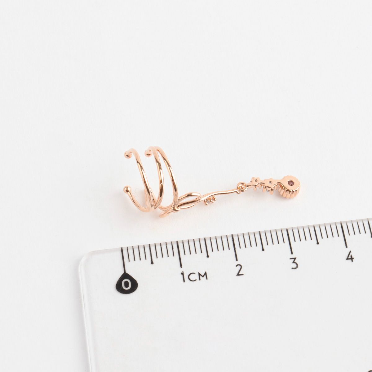 Rose gold ear cuff with a small chain on a white background with a ruler for scale.