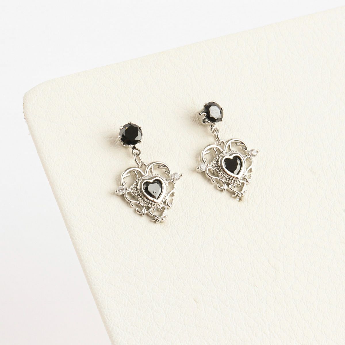 Heart-shaped earrings with black gemstones on a white cushion