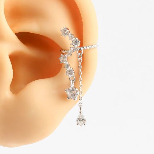 Silver earring with clear gemstones worn on an ear against a white background