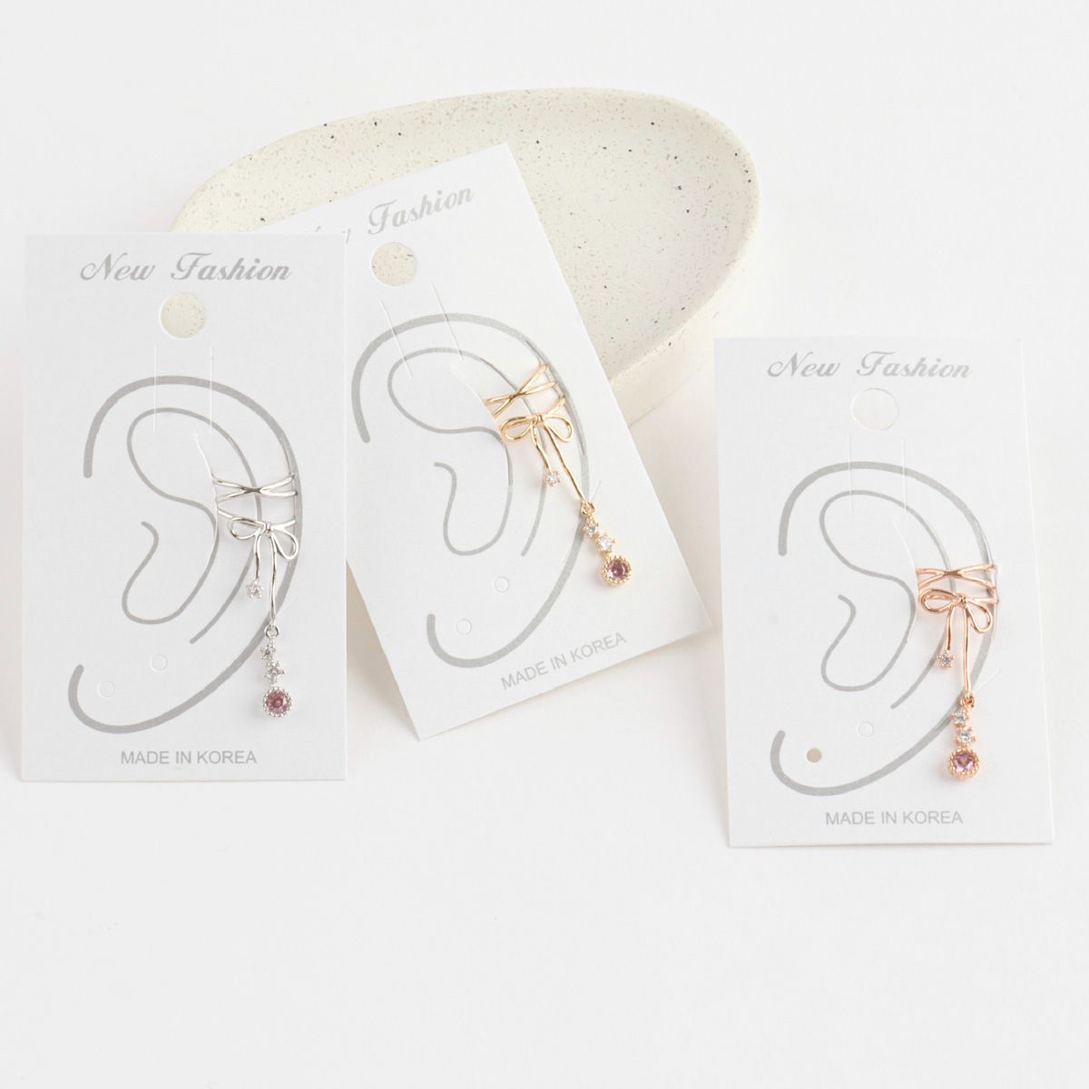 Pair of gold bow-shaped earrings on display cards with 'Made in Korea' text.