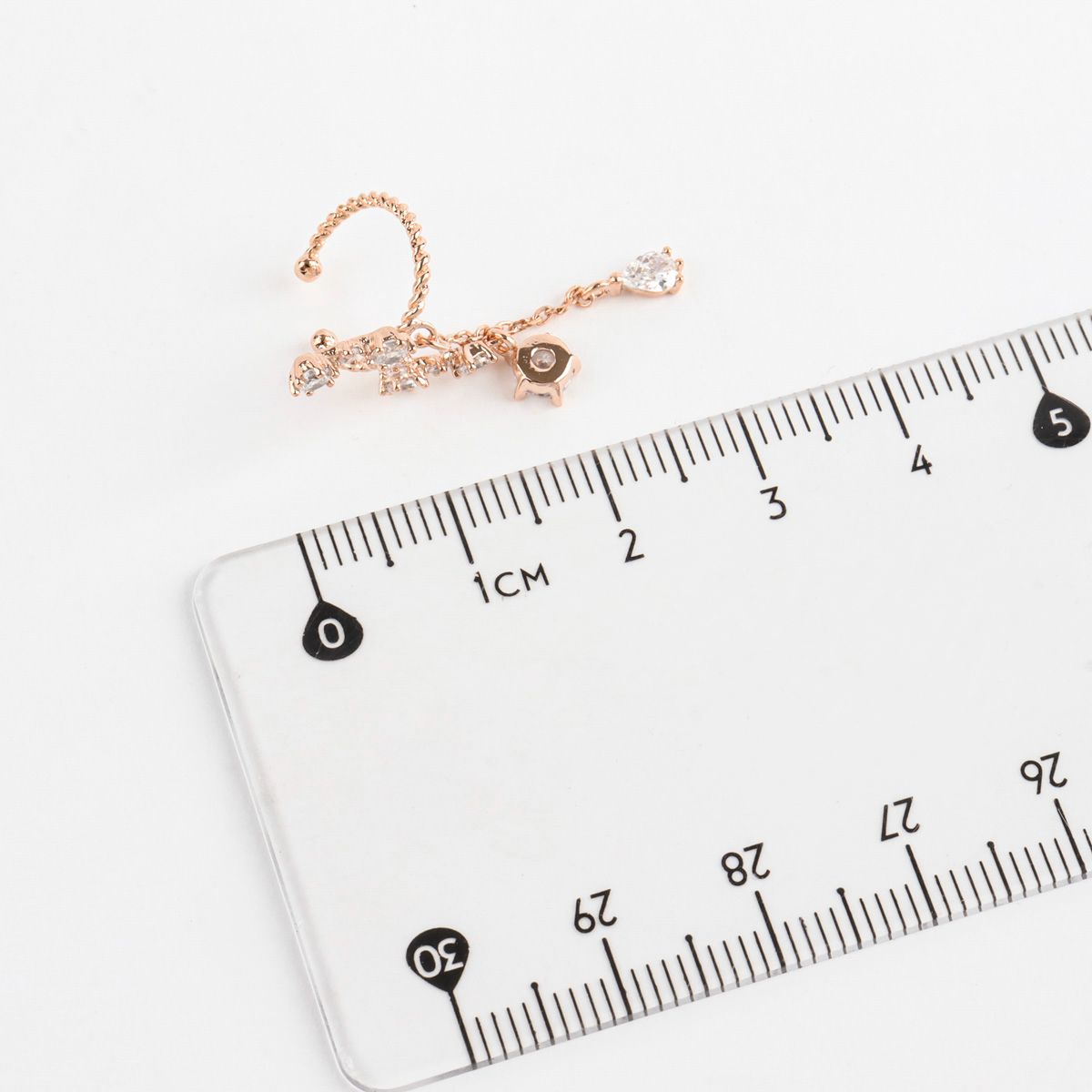 Rose gold ear cuff with a clear ruler for measurement on a white background