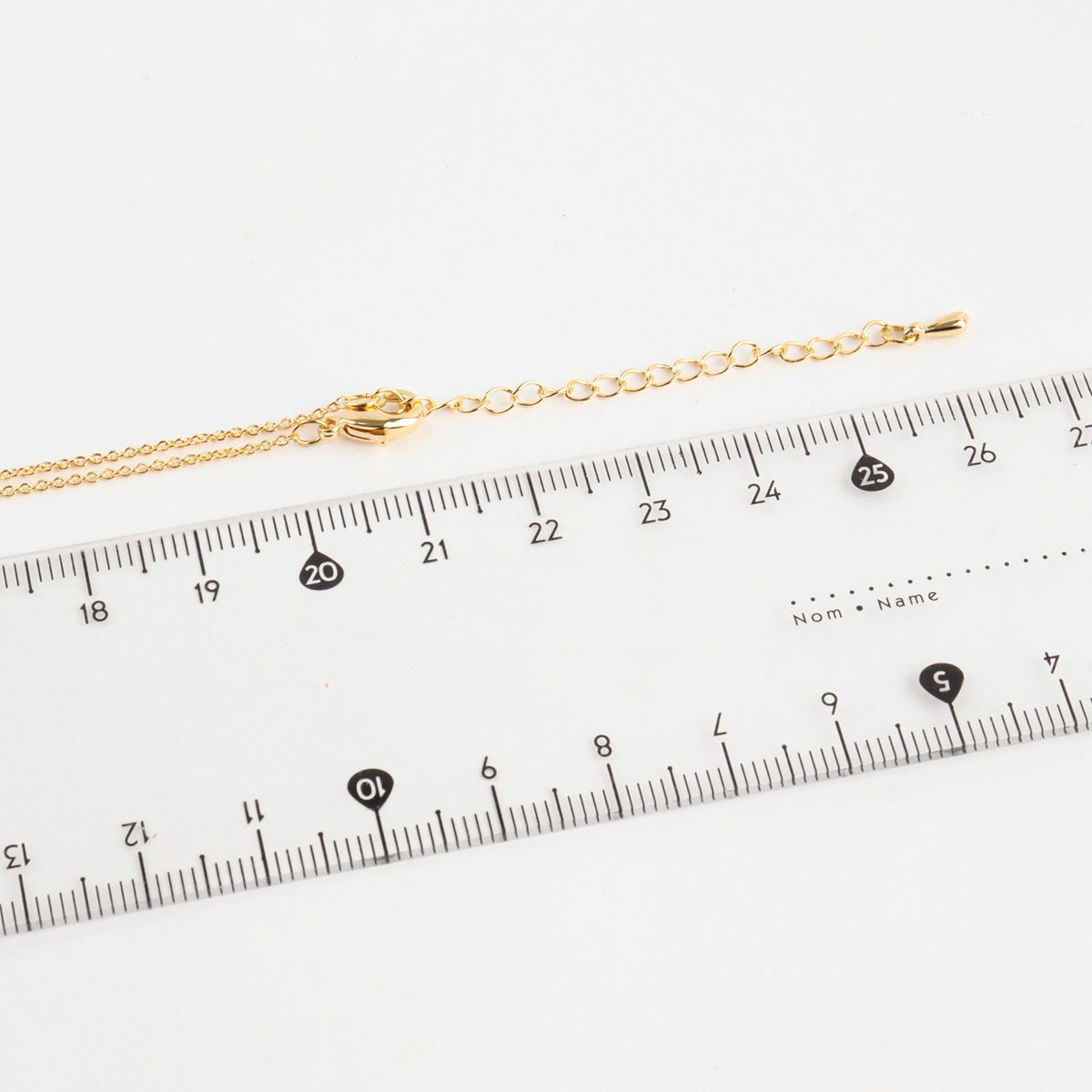 Gold bracelet on a ruler for size measurement against a white background