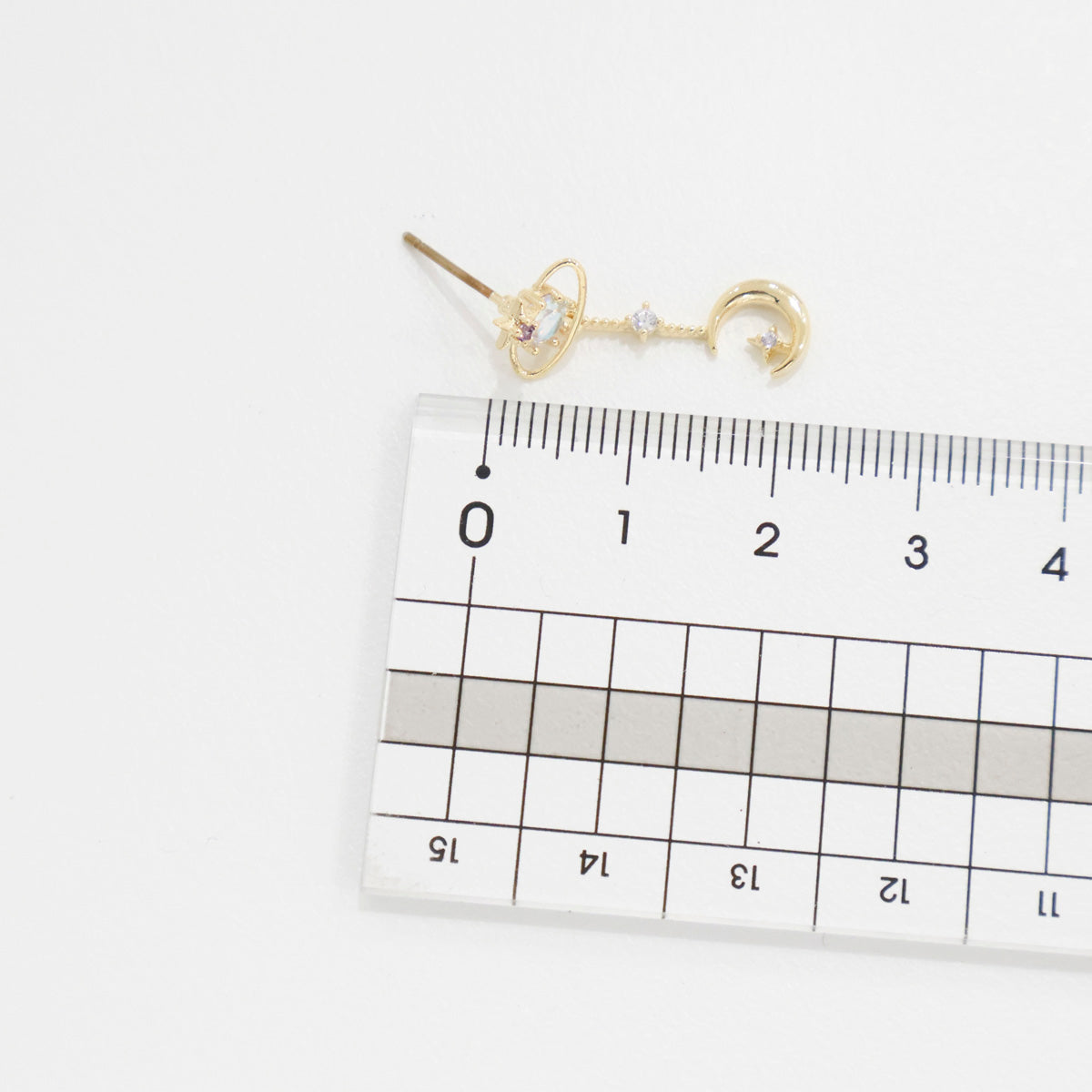 Gold key-shaped earrings on a ruler for size reference