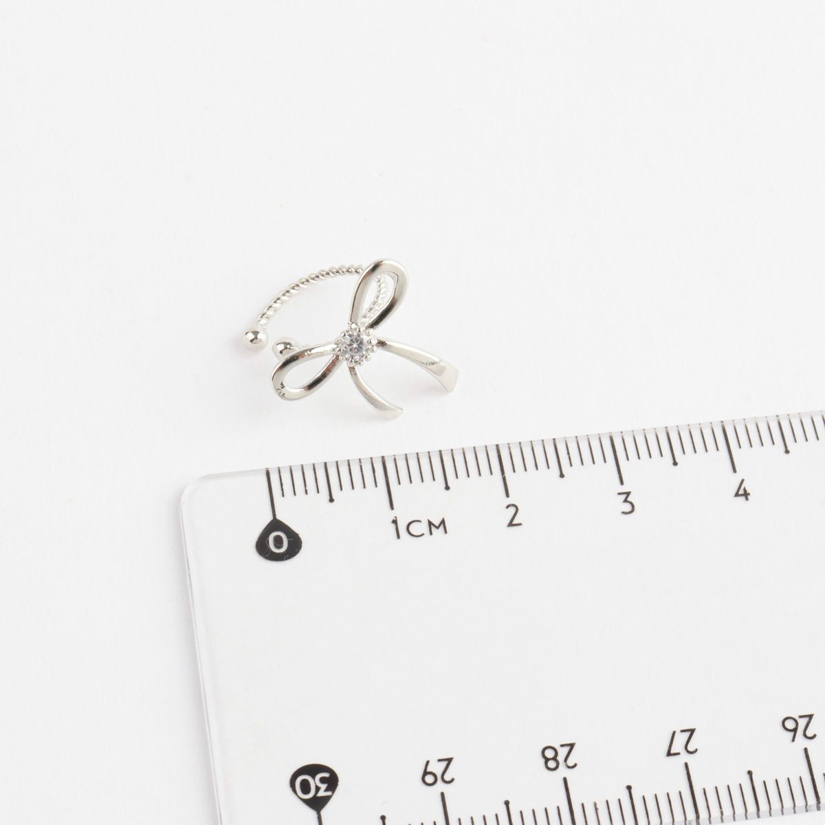 Silver bow-shaped ring on a ruler for size reference