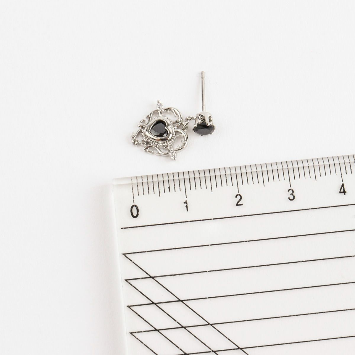 Silver earrings with a black heart-shaped gemstone on a ruler for scale.